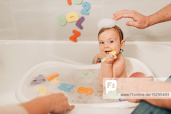 Mother and father putting bath suds on baby daughter's head  cropped