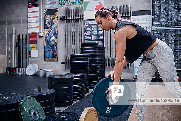 Young woman lifting weight plate in gym