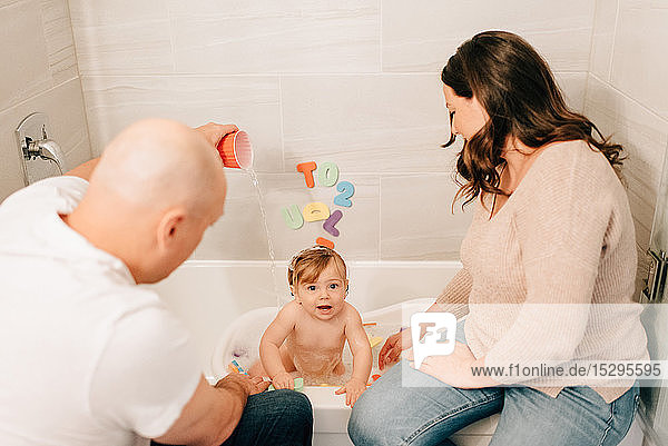 Mutter und Vater gießen Wasser in die Badewanne ihrer Tochter
