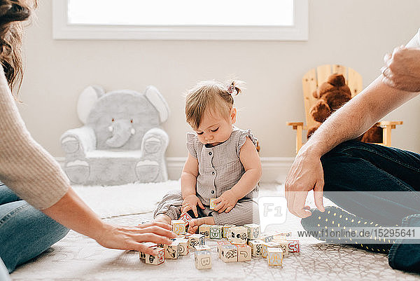 Mother and father on nursery floor with baby daughter playing with building blocks  cropped