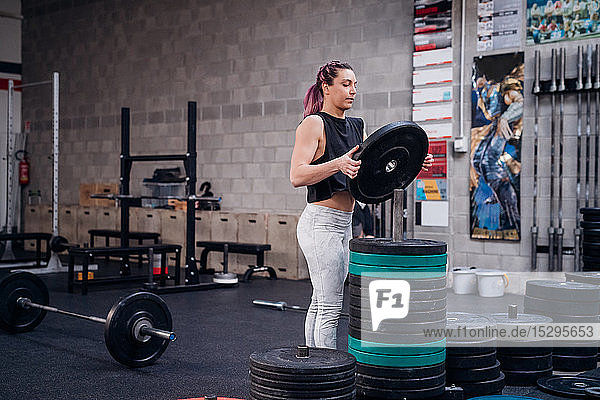 Young woman placing weight plate onto rack in gym