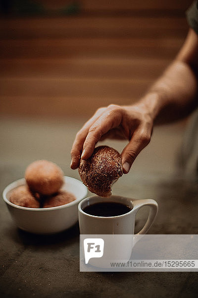 Mann taucht Doughnut in schwarzen Kaffee an Café-Tisch  abgeschnittener flacher Fokus