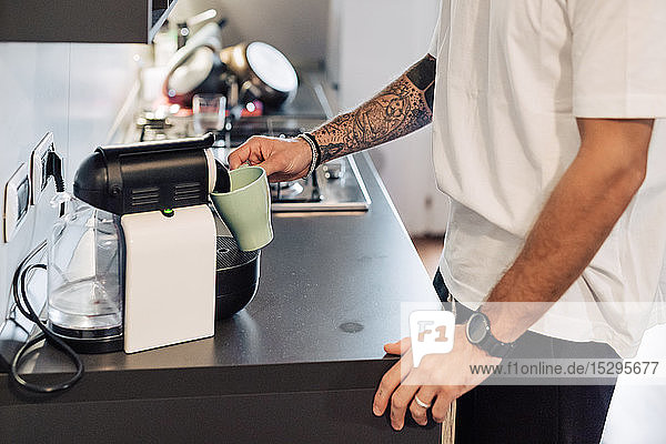 Mittlerer erwachsener Mann  der Kaffee aus der Kaffeemaschine auf der Küchentheke ausschenkt  mittlerer Abschnitt