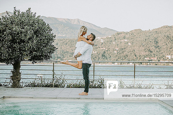Romantic mid adult man lifting up girlfriend on poolside  portrait  Stresa  Piemonte  Italy