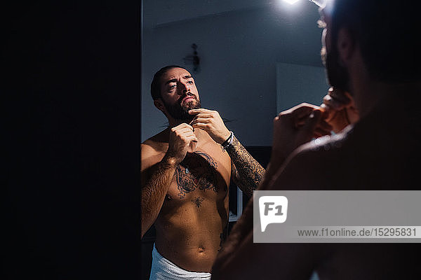 Mittelgroßer erwachsener Mann mit Tattoos  die den Bart am Badezimmerspiegel beschneiden
