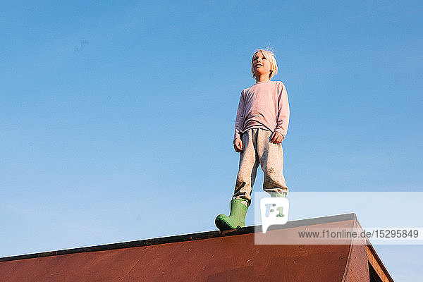 Junge steht oben auf der Skateboard-Rampe vor blauem Himmel  Blick aus niedrigem Winkel