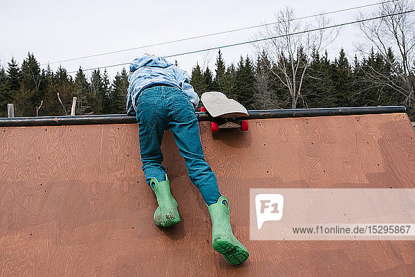 Junge klettert auf die Spitze der Skateboard-Rampe  Rückansicht