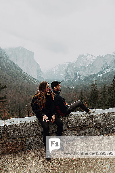 Junges Paar sitzt auf einer Mauer in einer Berglandschaft  Yosemite Village  Kalifornien  USA