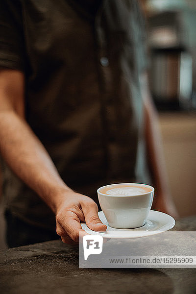 Barista stellt Tasse Milchkaffee auf Café-Theke  abgeschnittener flacher Fokus