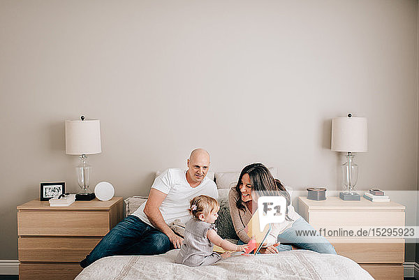 Mother and father on bed with baby daughter looking at story book