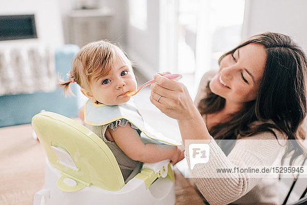 Mother feeding baby daughter in child seat  portrait