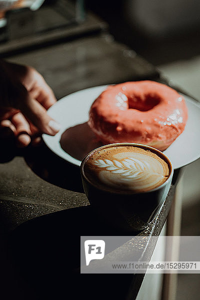 Barista legt Ring-Doughnut bei einer Tasse Milchkaffee auf die Café-Theke  niedriger Schwerpunkt