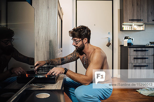 Mittelgroßer erwachsener Mann mit Tätowierungen  der Vinyl auf einem Plattenspieler spielt