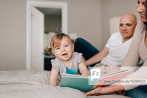 Mutter und Vater im Bett mit Baby-Tochter mit Geschichtenbuch  Porträt