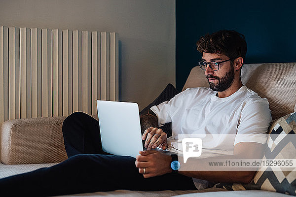 Mittelgroßer erwachsener Mann sitzt auf dem Sofa und tippt am Laptop