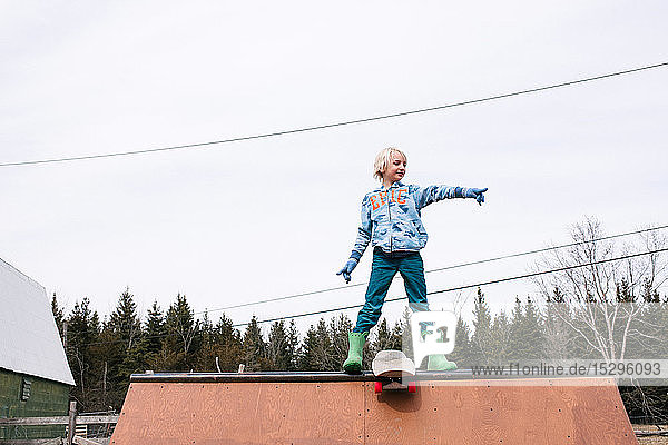 Junge steht oben auf der Skateboard-Rampe und zeigt