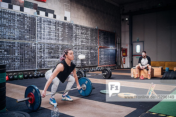 Young man watching woman lift barbell in gym
