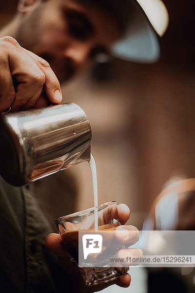 Barista pouring milk into coffee glass in cafe  close up of hands