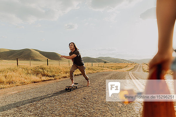 Young barefoot male skateboarder skateboarding on rural road  girlfriend watching  Exeter  California  USA