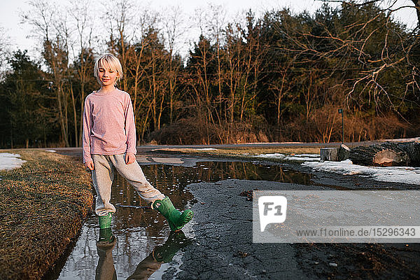 Junge steht knöcheltief in ländlicher Schmelzwasserpfütze  Porträt