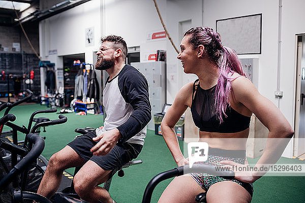 Exhausted young woman and man training together on gym exercise bikes  taking a break