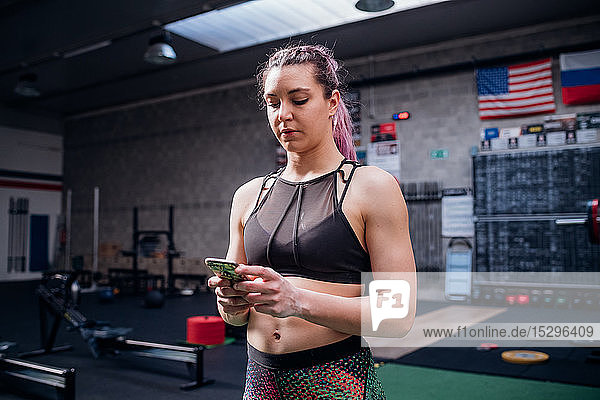Junge Frau beim Training  Blick auf Smartphone im Fitnessstudio