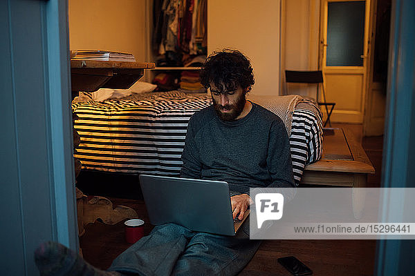 Bärtiger junger Mann benutzt Laptop im Schlafzimmer