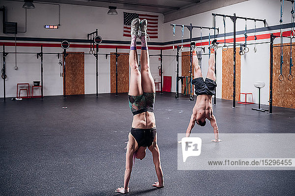 Junge Frau und Mann trainieren zusammen  machen Handstand im Fitnessstudio