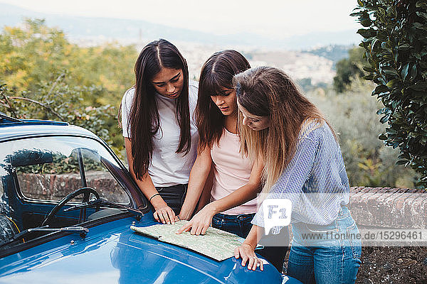 Friends reading route map on car bonnet in countryside