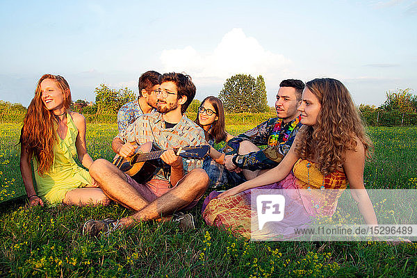 Group of young adults sitting in field listening to acoustic guitar