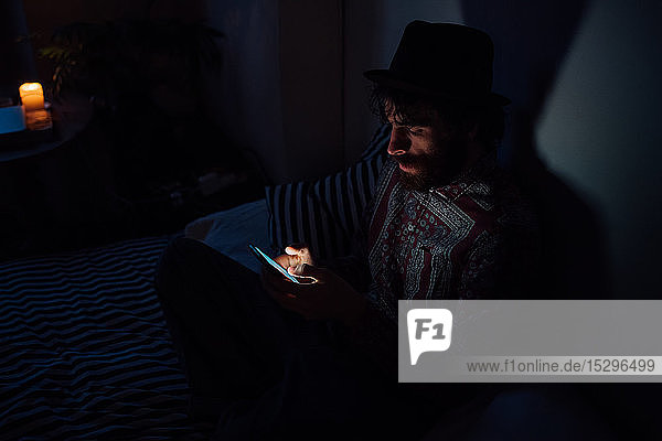 Bärtiger junger Mann benutzt Smartphone in dunklem Raum