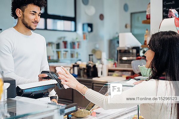 Young businesswoman making smartphone payment at cafe counter