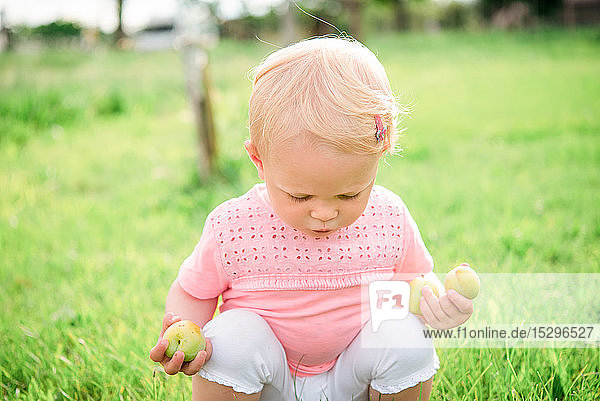 Süßes weibliches Kleinkind hockt auf Gras und schaut nach unten