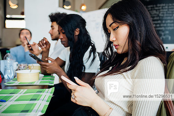 Männliches und weibliches Geschäftsteam betrachtet Smartphones während des Arbeitsessens am Café-Tisch