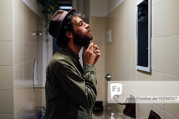 Bärtiger junger Mann beim Bartstreichen im Badezimmer