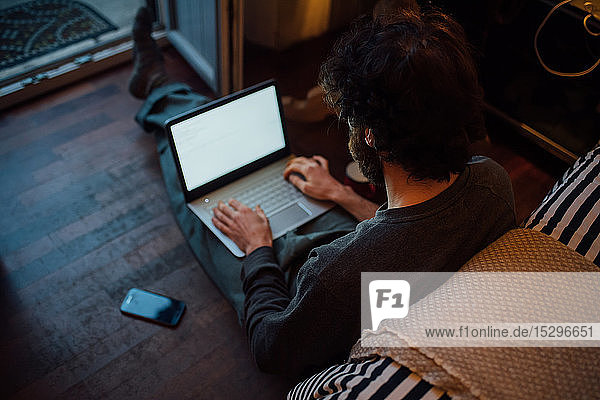 Bärtiger junger Mann benutzt Laptop im Schlafzimmer