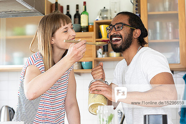 Woman feeding man with wooden spoon in kitchen