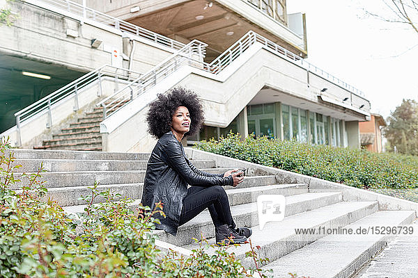 Junge Frau mit Afro-Haaren sitzt auf einer Stadttreppe und schaut weg