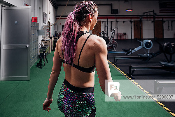 Young woman with plaited purple hair walking through gym