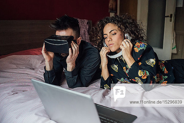 Couple using VR headset and laptop on bed