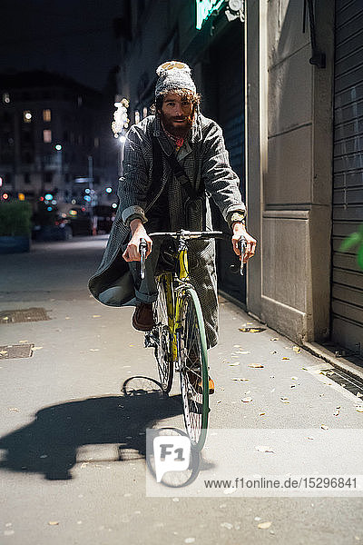 Bärtiger junger Mann fährt Fahrrad auf dem Bürgersteig