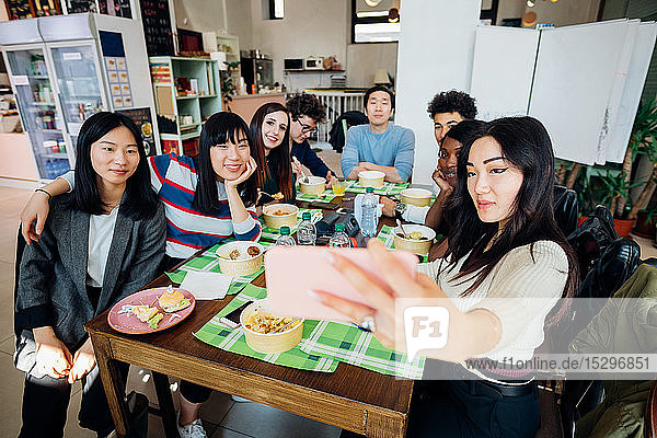 Junges männliches und weibliches Geschäftsteam beim Arbeitsessen am Café-Tisch  mit Smartphone-Selfie
