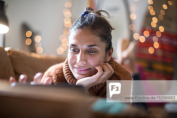 Junge Frau liegt auf dem Wohnzimmersofa und schaut auf den Laptop  Nahaufnahme