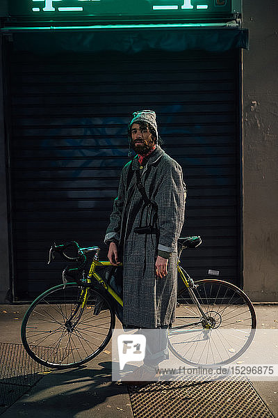 Bärtiger junger Mann mit Fahrrad auf dem Bürgersteig