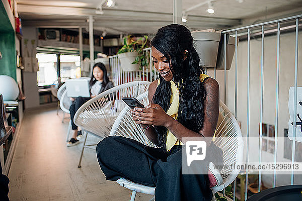Junge Geschäftsfrau betrachtet Smartphone im Cafe
