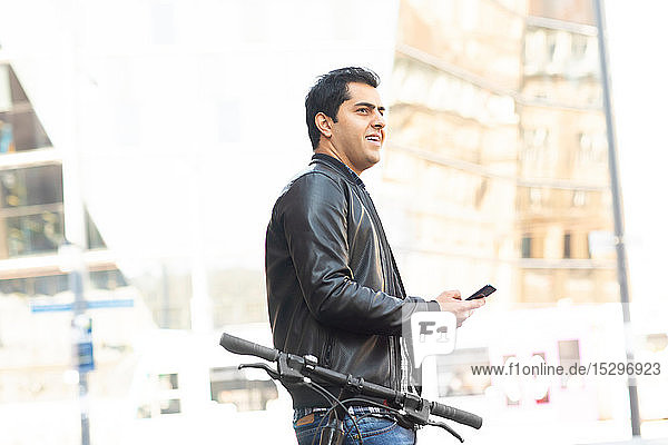 Young man using smartphone beside bicycle in city