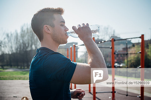 Gymnastik im Fitnessstudio im Freien  junger Mann trinkt Wasser in Flaschen