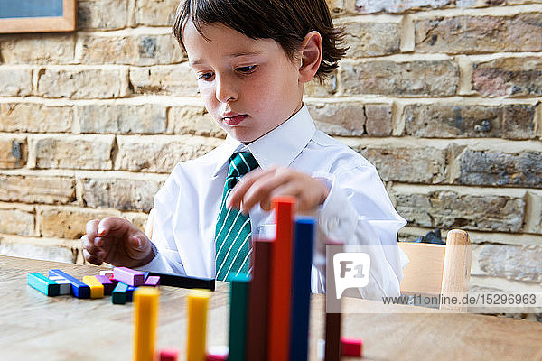 Junge in Schuluniform spielt zu Hause mit farbigen Stöcken