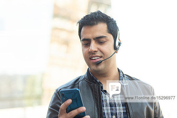 Young man using smartphone with bluetooth headset