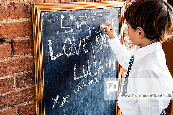 Junge in Schuluniform schreibt zu Hause an Tafel